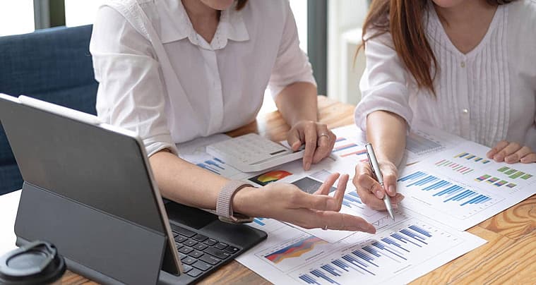 Dos personas analizando gráficos de datos coloridos y reportes financieros sobre un escritorio de madera.